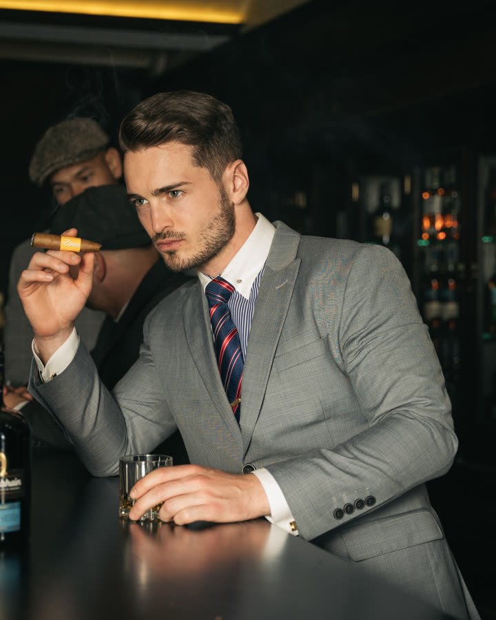 Andreas Schmid, grey suit with a cigar and a glass at a bar