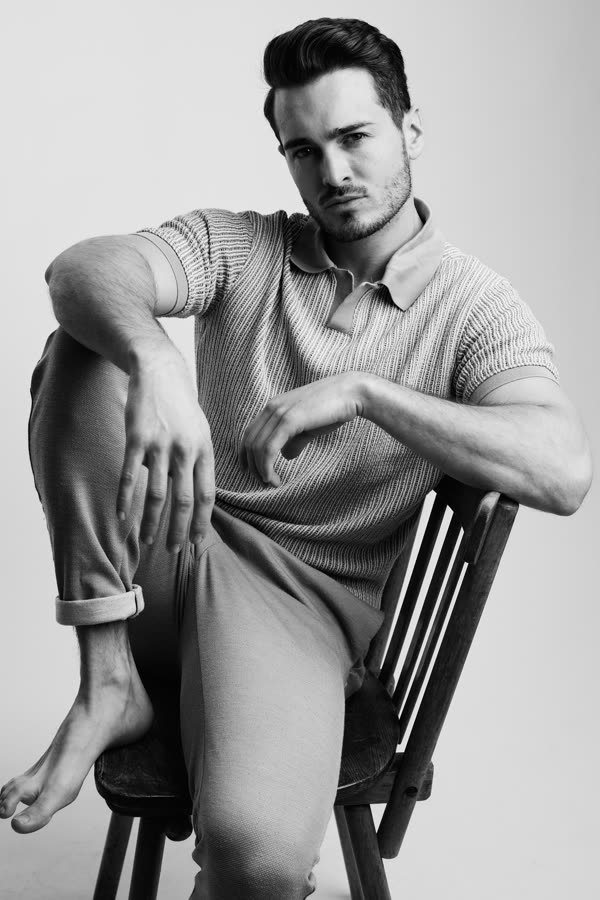 Andreas Schmid, black and white studio photo in a knitted polo on a chair