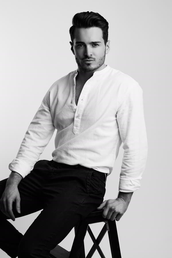 Andreas Schmid, black and white studio photo, seated on a stool