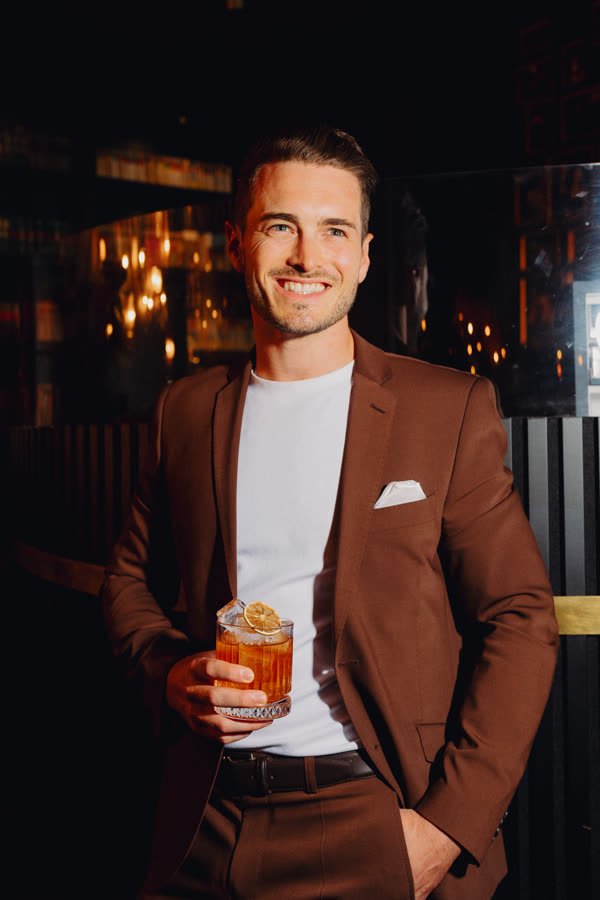 Andreas Schmid, rust brown suit with a drink in a bar